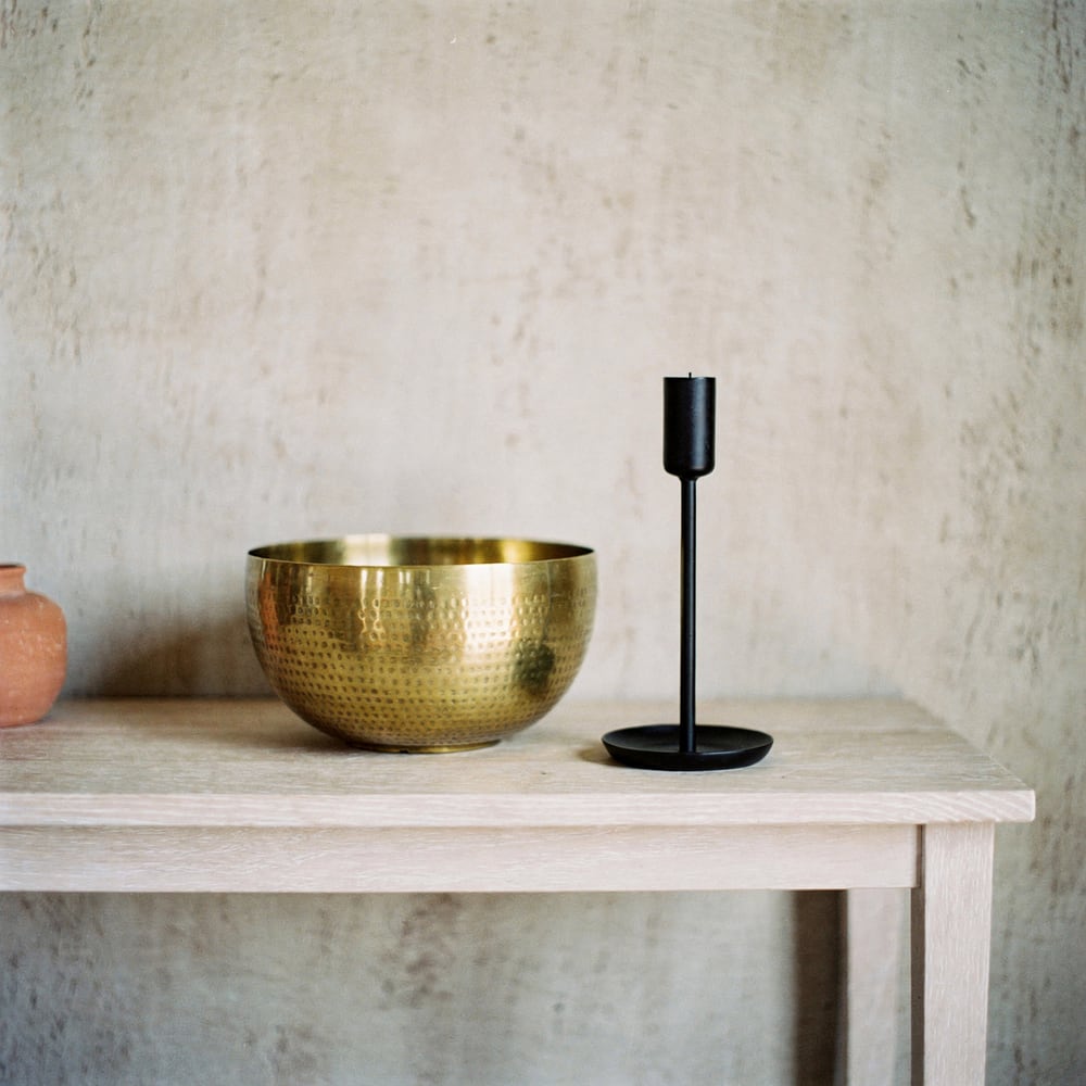 Hammered brass bowl and iron candle holder on an oak console, rendered
